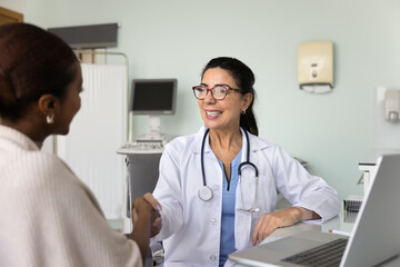 Positive doctor giving handshake to patient after consultation, smiling. Happy confident medical professional shaking hands with young African woman after effective therapy and recovery