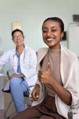 Cheerful beautiful young African patient woman recommending clinic, showing thumb up like approval...