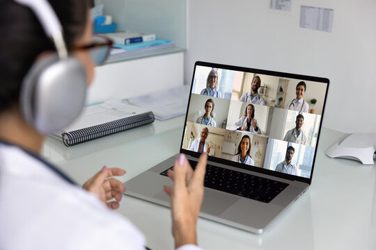 Female doctor in headphones speaking on telemedicine conference, talking to team of colleagues in group video call, holding training webinar, giving learning lecture. Laptop screen over shoulder view