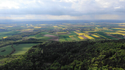 A  aerial view of vast green fields and rolling hills in spring. The scenic landscape with a patchwork of farmland under a cloudy sky is perfect for nature and travel themes.