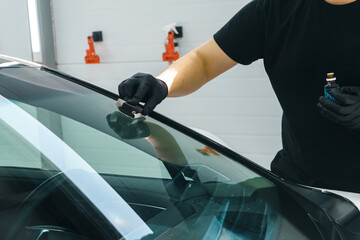 A master in black gloves applies a nano protective coating to a car windshield.