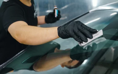 A master in black gloves applies a nano protective coating to a car windshield.