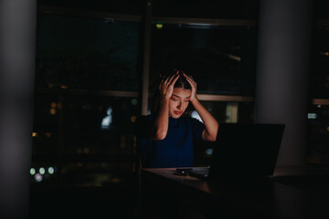 A businesswoman looks stressed while working late at night on a laptop in a dimly lit office. The image conveys feelings of exhaustion, dedication, and the challenges of late-night work.