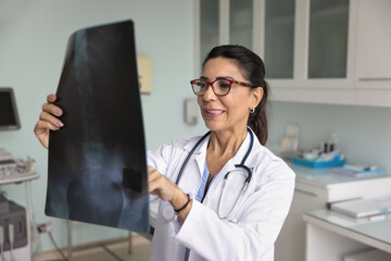 Positive senior trauma surgeon doctor woman examining mri scan image of spine and pelvic bones,...