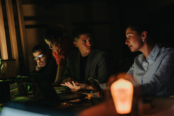 A group of business people working diligently on a project in a dimly lit office. The atmosphere portrays focus and teamwork as they collaborate late into the night to meet deadlines.