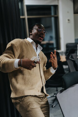 A young businessman wearing glasses and a sweater strikes a lively pose in a contemporary office environment, capturing a relaxed and casual vibe during a work break.