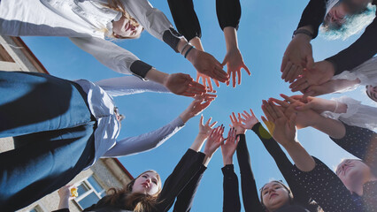 Students come together in a circle with their hands against a clear blue sky, showcasing teamwork and unity