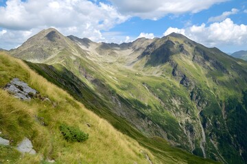 Fototapeta premium Mountain peaks reach skyward, green slopes under a partly cloudy sky