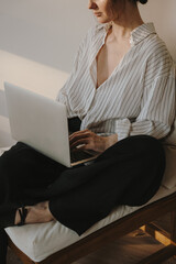 Focused woman working on laptop, casual striped shirt, bright minimalist living room, natural...