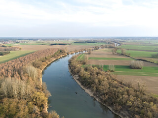 Obraz premium Aerial view of a picturesque river winding through lush green fields and woodland, showcasing the beautiful landscape during daylight in spring.