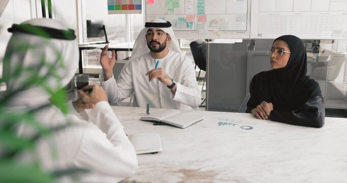 Middle-Eastern team discuss project gathered in conference room, considering financial investment opportunities or partnerships, analyze progress, collaborate on joint project, evaluate revenue growth