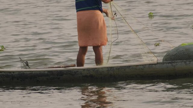Fisherman skillfully casting a net from a canoe into tranquil waters