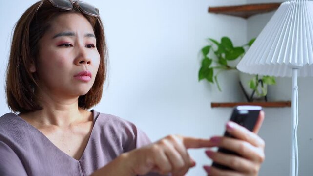 middle-aged asian woman, 45 years old, struggling to read small text on her phone screen due to farsightedness, squinting her eyes and holding the phone farther away because of blurry vision
