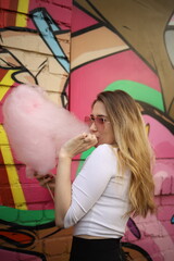 In a colorful urban environment, a young woman with long hair is savoring cotton candy while...