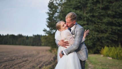 Romantic newlyweds sharing passionate kiss, embracing amid lush greenery with woodland backdrop symbolizing wedding day intimacy