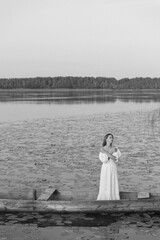 A woman in a white dress stands in a wooden boat among water lilies on a quiet lake. The evening...