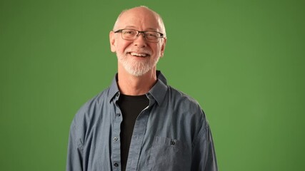 A mature man stands smiling, raising his hand in a friendly wave. He wears a casual outfit and conveys a warm, cheerful emotion against a solid green backdrop.