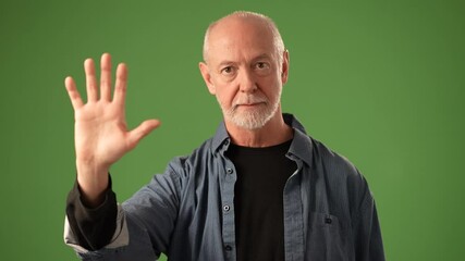 A mature man stands against a solid green background, raising his hand in a gesture that says Stop. His expression reflects wisdom and experience.