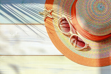 Summer hat and sunglasses on a wooden background with a palm shadow. Summer vacation concept. Top view, copy space.