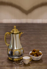 Traditional Arabic coffee dallah with golden accents alongside a porcelain cup, a bowl of delicious dates, and prayer beads set on an elegant wooden table, representing Middle Eastern hospitality.