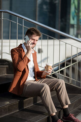 Fototapeta premium Businessman sitting in the city using a cellphone and holding coffee.