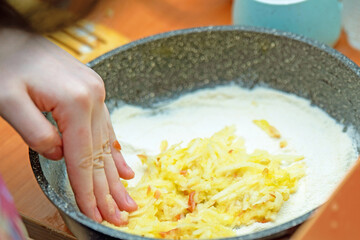 hand carefully spreads a layer of mashed apples into a pie dish, preparing for a delicious homemade apple pie. The warm, inviting colors evoke a sense of comfort and tradition