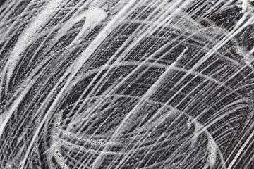 Foam and soap streaks on dark surface. Cleaning texture with abstract swirl pattern. White detergent traces close up. Sanitary background concept. Car wash or hygiene cleaning process detail.