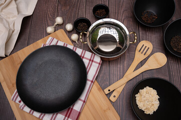 Aesthetic Flat Lay of Kitchen Essentials Featuring a Black Plate, Wooden Utensils, Cutting Boards, Spices, Garlic, and a Stainless Steel Pot on a Rustic Wooden Surface with a Cozy Culinary Atmosphere