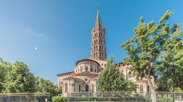 The cobbled parvis of the Basilica of Saint Sernin in Toulouse, France, timelapse hyperlapse. Largest romanesque church in Europe with brick bell tower, arched doors, green trees and blue sky