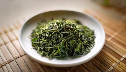 Loose Tea - A small, white ceramic dish holding a neat pile of loose green tea leaves, captured in soft lighting