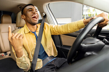 Emotional black guy having fun while driving car, listening to music and singing, moving his hand, shot from inside
