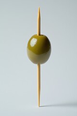 Solitary green olive impaled on a wooden toothpick against a soft white background in a minimalist style with studio lighting and a high angle view