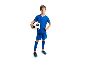 Confident boy in blue sport outfit posing with classic soccer ball over white background