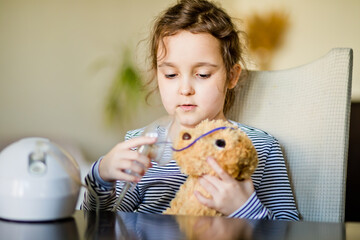 Sick little girl with cough doing inhalation at home with nebulizer inhaler mask. Asthma medicine....