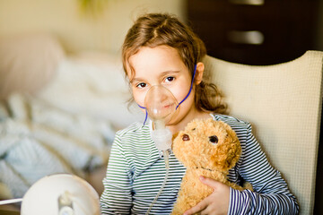 Sick little girl with cough doing inhalation at home with nebulizer inhaler mask. Asthma medicine....