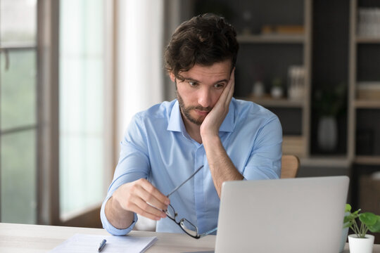 Mentally drained. Exhausted unmotivated bored gen z guy office worker student sit at desk stare at notebook screen feel tired of stressful unproductive dull work unable to solve too difficult problem