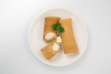 Golden-brown folded crepes with cottage cheese filling on a white plate, garnished with a sprig of...