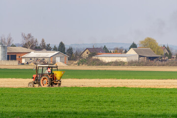 old tractor with attached seeder drives across the field. farmer's field work early spring. sowing...