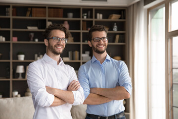 Fototapeta premium Cheerful and confident sibling duo. Happy smiling successful millennial twin brothers stand with arms crossed look forward proud to be team feel each other support with strong bond shared ideas dreams