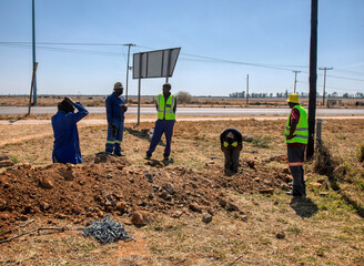group of African road construction workers shoveling digging a trench ditch on the side of the...