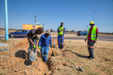 group of African road construction workers shoveling digging a trench ditch on the side of the...