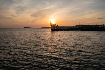 Silhouetted figures stand against setting sun at Blackrock platform as golden light ripples on water.