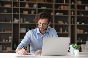 Preparing academic research. Concentrated young male student in glasses read statistic reports hold...