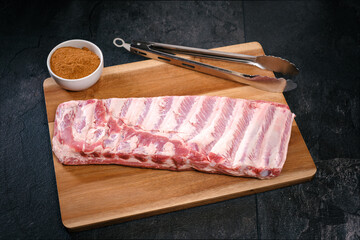 St. Louis Cut Rib, roh, Schale mit Gew&uuml;rz, Grillzange, auf Holzteller, Holzbrett, auf schwarzem Schiefer