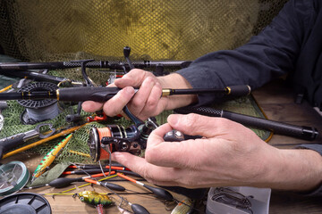 Fishing tackle on a table in a composition with fishing accessories. Close-up of hands. A fisherman checks his tackle for further use on a fishing trip. © vizafoto