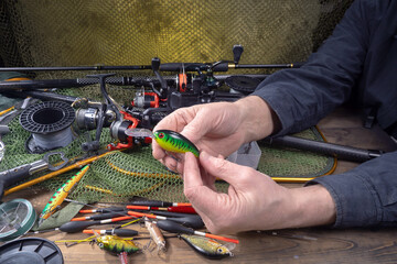 Sport fishing equipment on a table in a studio composition, against a background of a net. A fisherman's hands check the tackle for use.