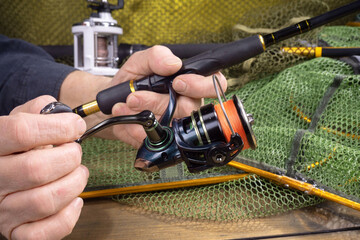 Sport fishing equipment on a table in a studio composition, against a background of a net. A fisherman's hands check the tackle for use.