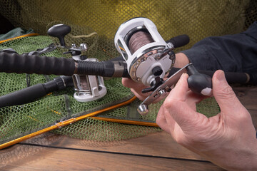 Sport fishing equipment on a table in a studio composition, against a background of a net. A fisherman's hands check the tackle for use.