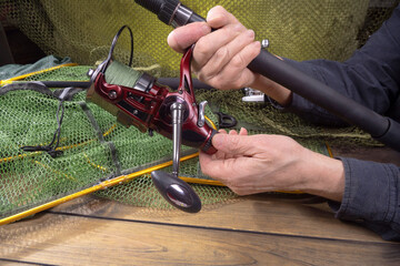 Sport fishing equipment on a table in a studio composition, against a background of a net. A fisherman's hands check the tackle for use.