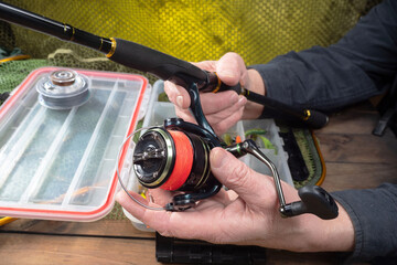 Sport fishing equipment on a table in a studio composition, against a background of a net. A fisherman's hands check the tackle for use.